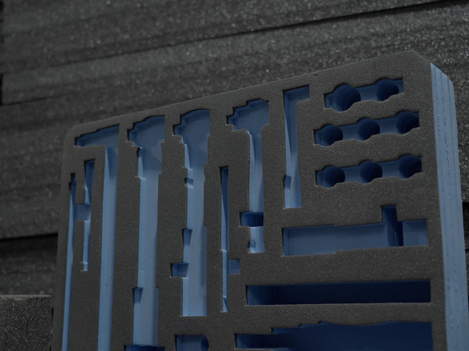 Close-up of a foam insert with long routed channels and round cavities over blue backing