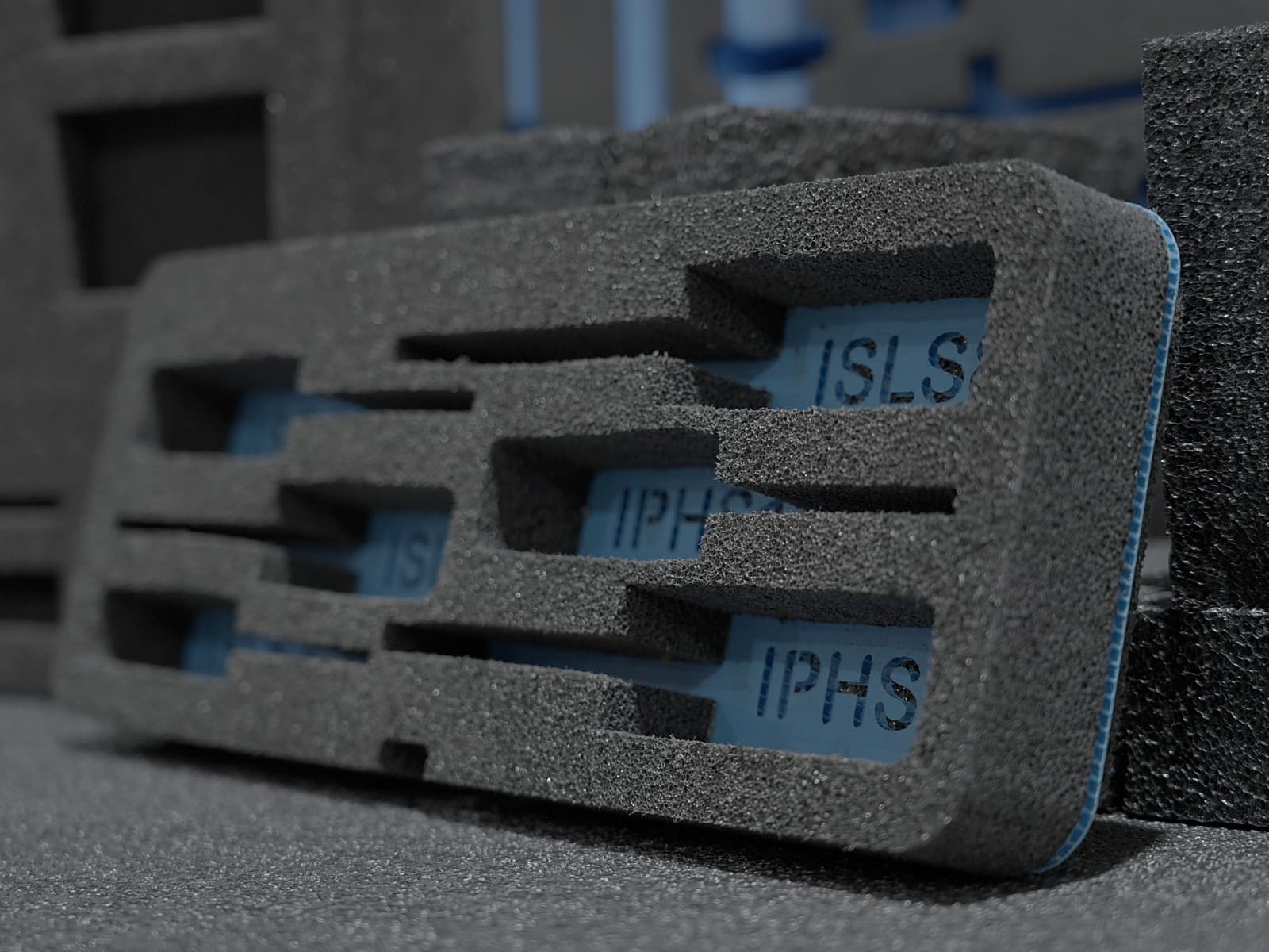 A routed foam insert with labeled cavities over blue backing, angled against stacked foam