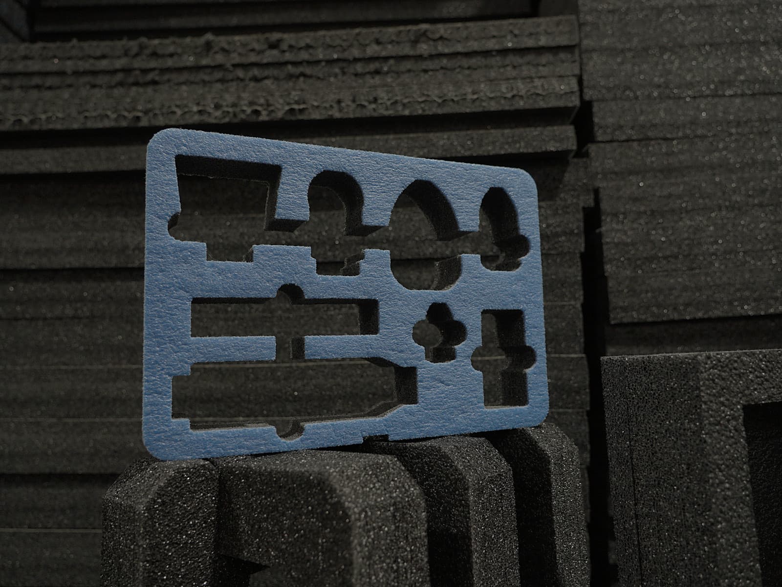 A foam insert panel with cut-out pockets standing against stacked foam sheets