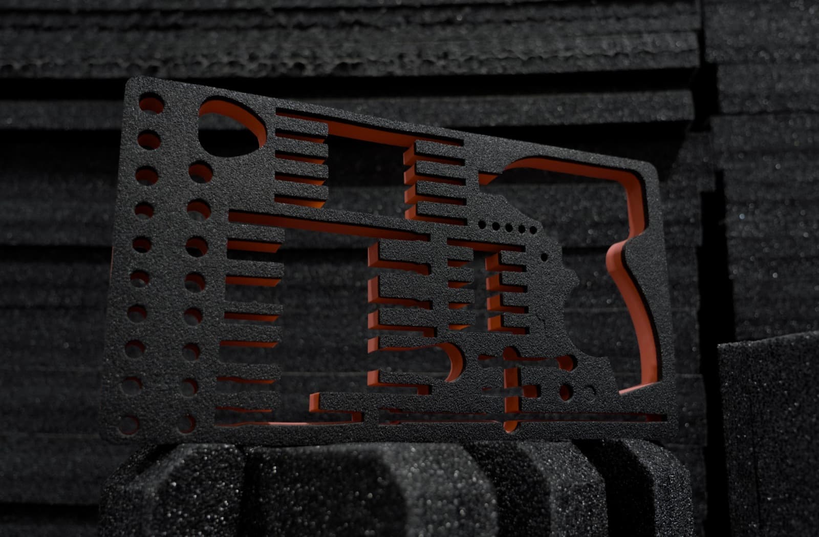 Intricately cut black foam insert with orange backing, held against stacked foam
